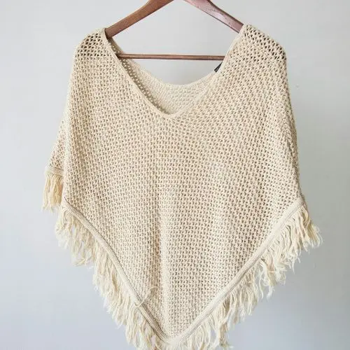 A stylish knitted poncho featuring fringes, hanging gracefully on a hanger, highlighting its craftsmanship