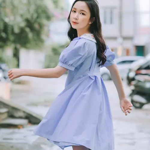 A woman in a blue dress strolls gracefully down a city street, surrounded by urban scenery.