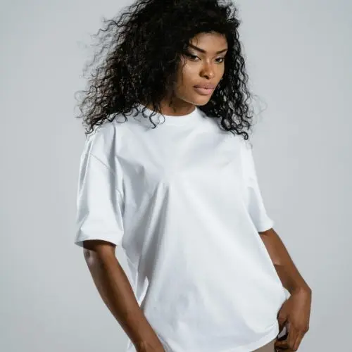 "Young woman with curly hair wearing a plain white t-shirt, posing against a light grey background."